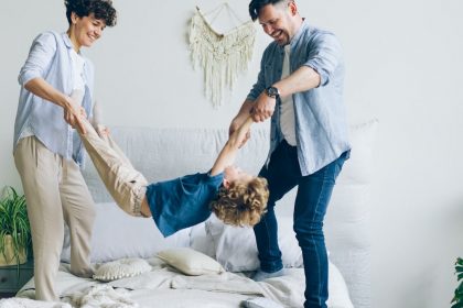 Mother father swinging child holding hands and feet then putting on bed at home