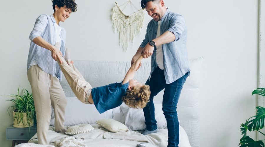 Mother father swinging child holding hands and feet then putting on bed at home