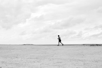 A lone runner traverses a vast, empty Brazilian beach under dramatic cloudy skies in black and white.